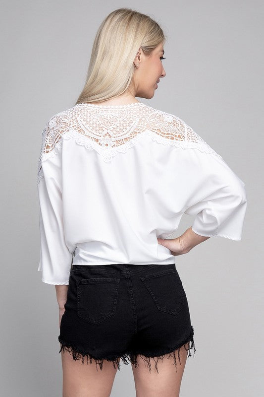 White blouse with lace trim, a tie neckline, and relaxed three-quarter dolman sleeves.