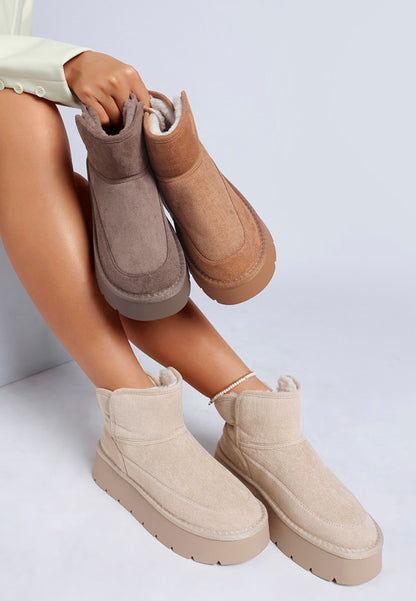 Woman wearing Sand Holias Chunky Heeled Snow Boots while holding Camel and Dark Grey variants together.