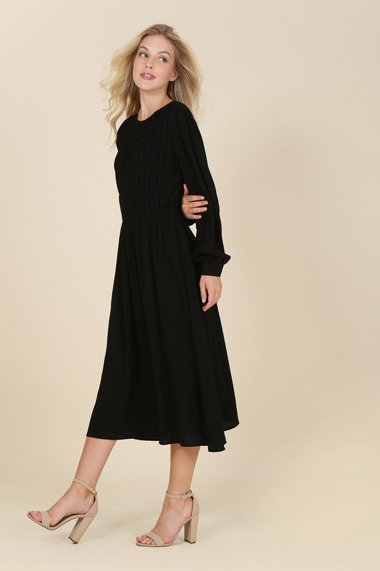 Black midi dress with a boat neck, ruched bodice, long sleeves, and buttoned cuffs. Made from crinkle fabric.