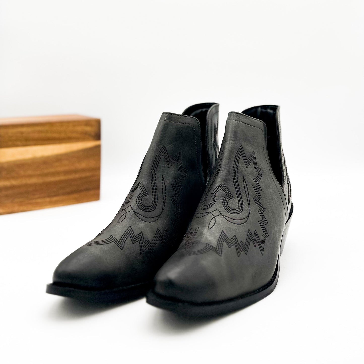 Black leather booties with Western embroidery, roomy snip toe, cushioned footbed, and ankle slits.