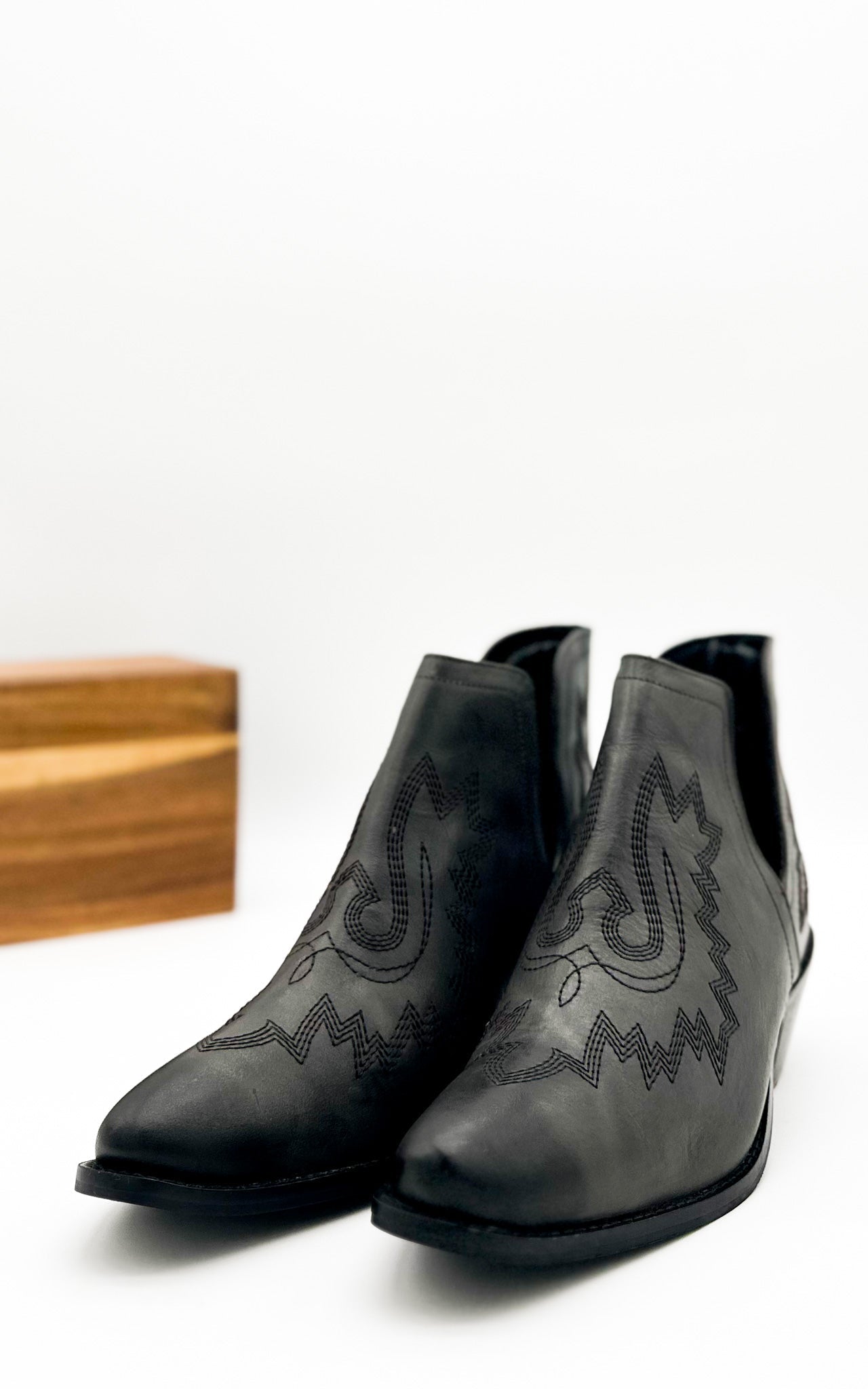 Black leather booties with Western embroidery, roomy snip toe, cushioned footbed, and ankle slits.