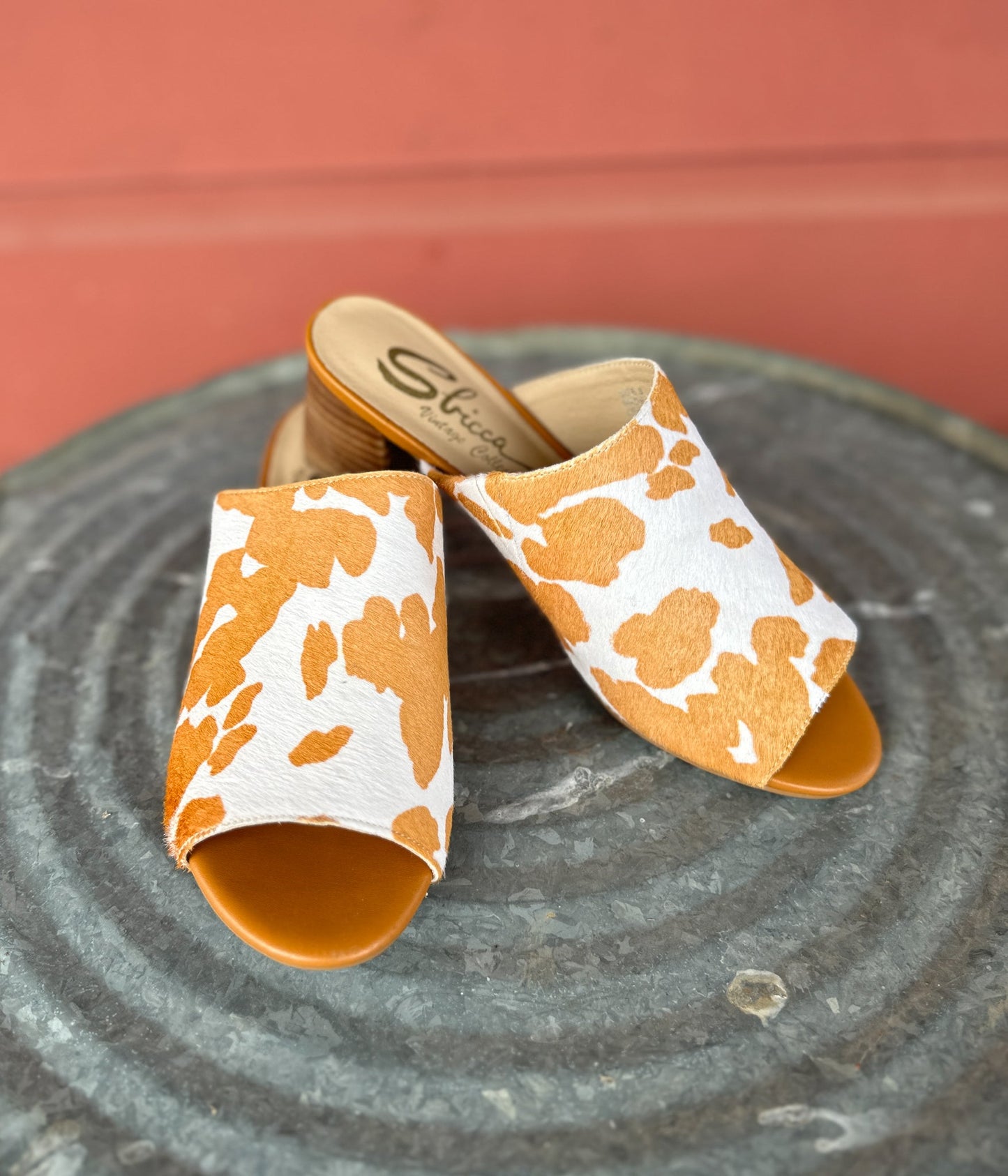 Tan and white cow print mule shoes for women, featuring a genuine calf-hair upper, synthetic lining, padded insole, and internal elastic gore for comfort. Designed with a low stacked leather heel, these slip-on mules are perfect for pairing with jeans, jumpsuits, or other outfits to add a playful, bold touch.