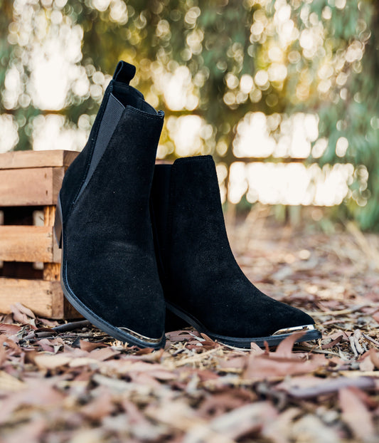 Women's black ankle booties made of genuine suede with a leather lining, featuring a slight pointed toe with a silver accent, 1.5-inch heel, pull-on style with elastic side panels and a pull tab. 