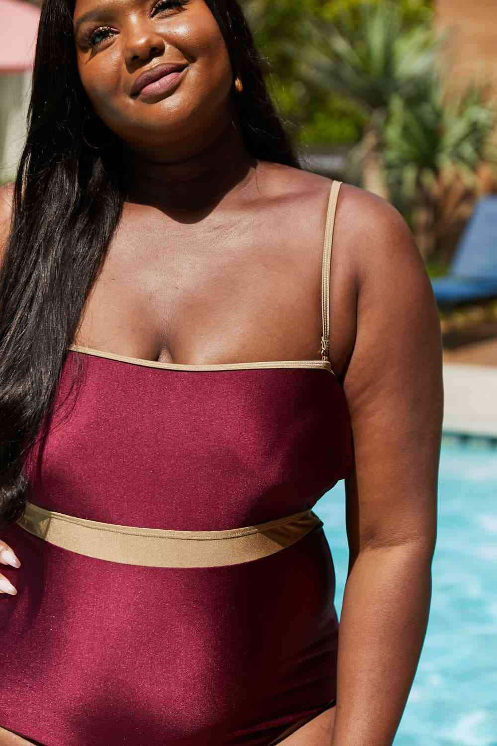 Wine-colored one-piece swimsuit with a contrast waistband, open back, shiny fabric, and a straight neckline.