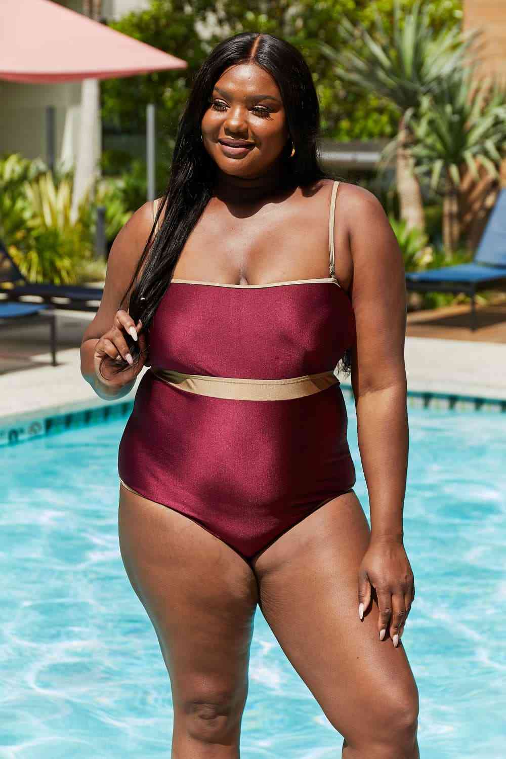 Wine-colored one-piece swimsuit with a contrast waistband, open back, shiny fabric, and a straight neckline.