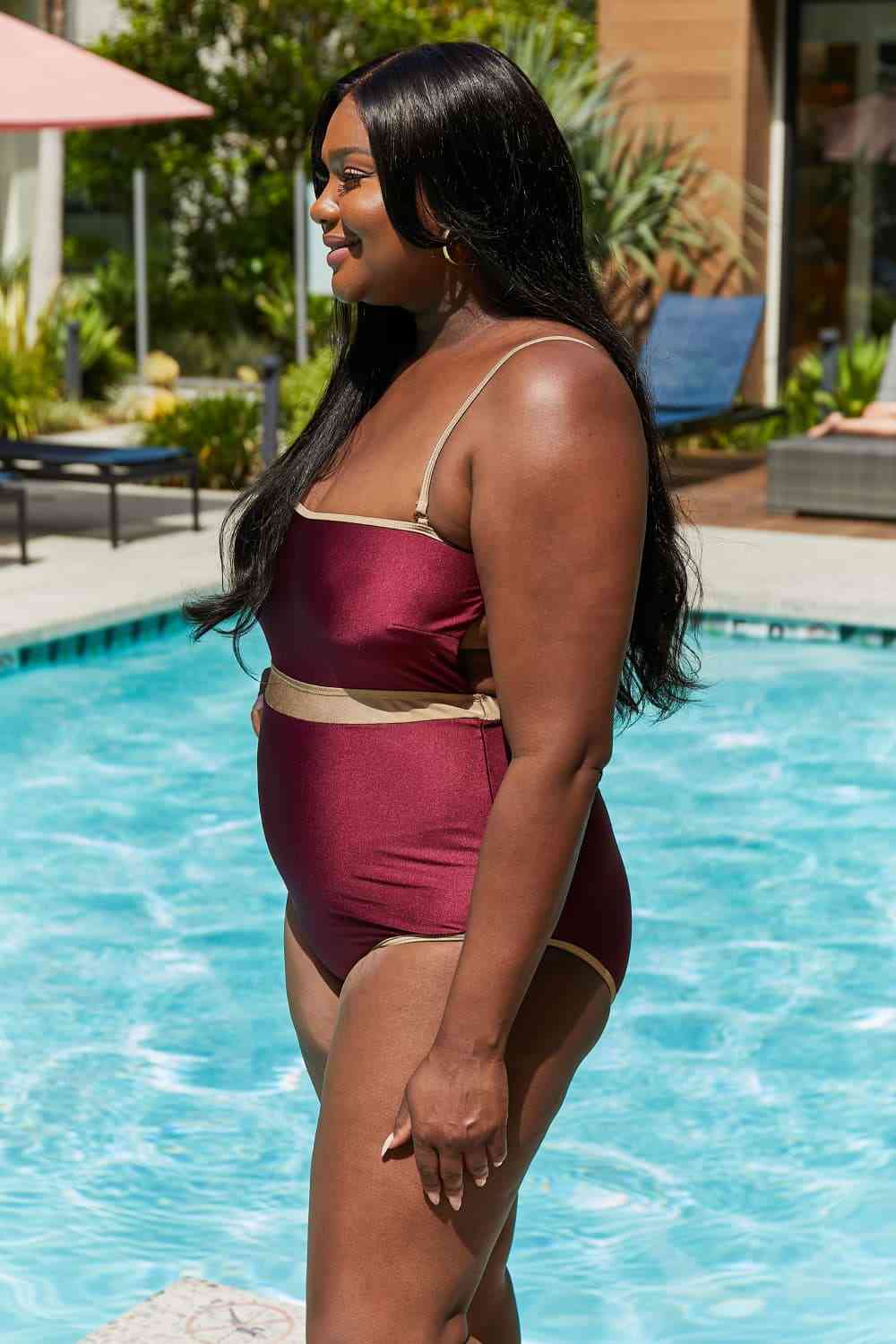 Wine-colored one-piece swimsuit with a contrast waistband, open back, shiny fabric, and a straight neckline.