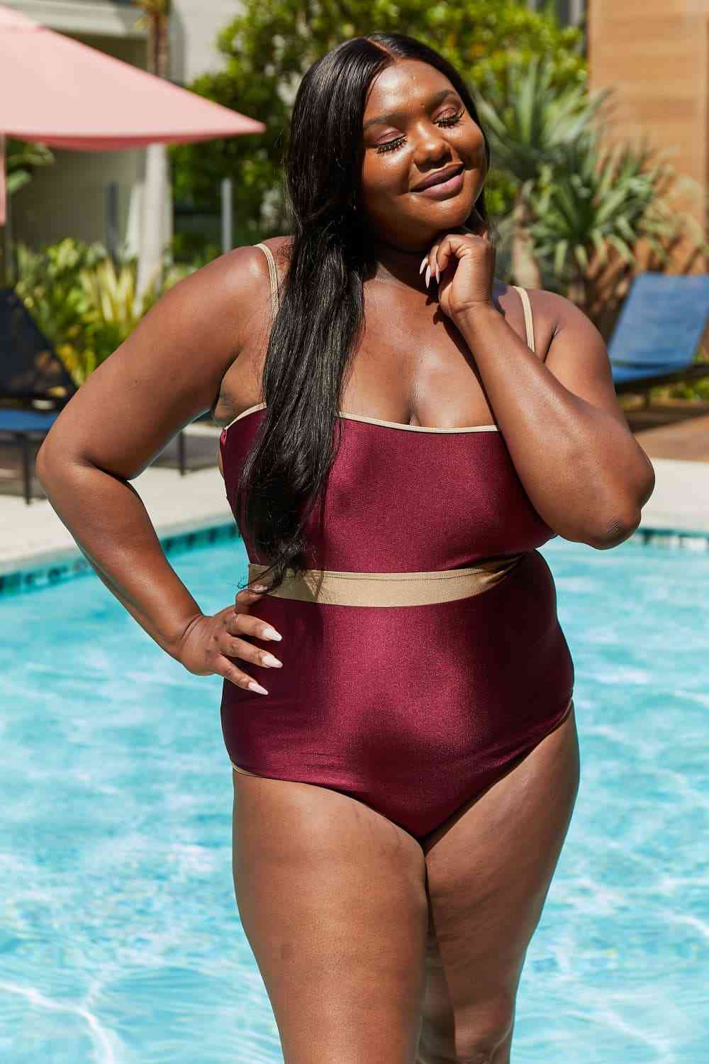 Wine-colored one-piece swimsuit with a contrast waistband, open back, shiny fabric, and a straight neckline.