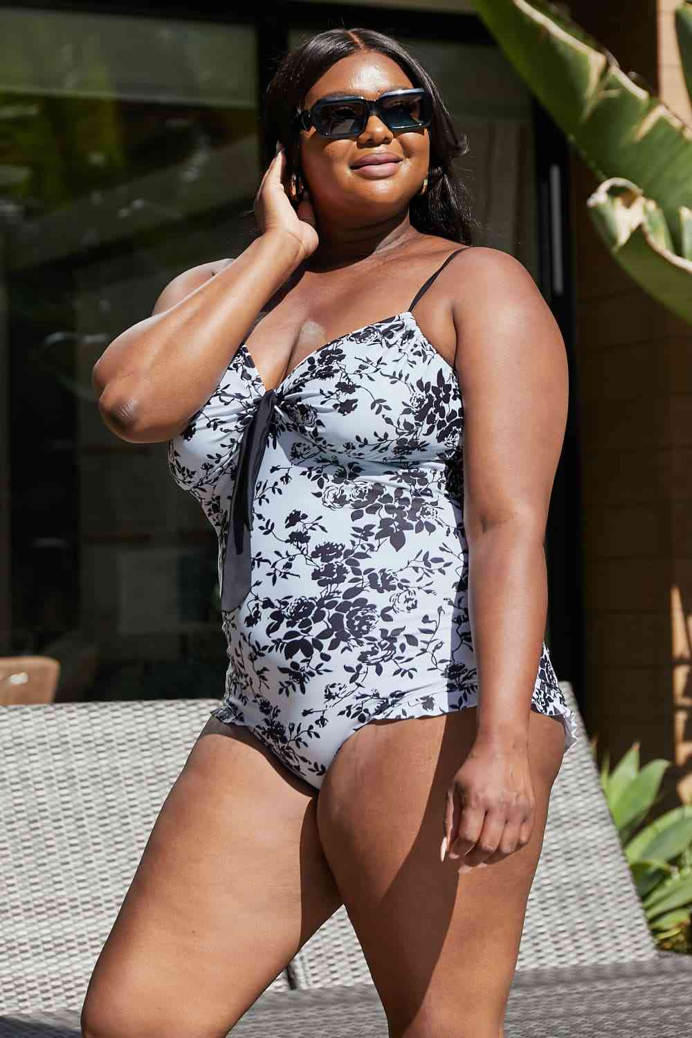 A vintage-style one-piece swimsuit with a toile floral pattern, bows, frilly trim, and a sweetheart neckline. It features adjustable straps, removable pads, and frills at the leg openings for extra coverage. 