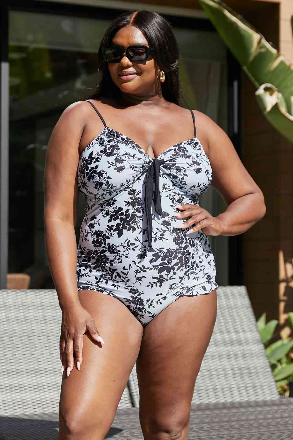 A vintage-style one-piece swimsuit with a toile floral pattern, bows, frilly trim, and a sweetheart neckline. It features adjustable straps, removable pads, and frills at the leg openings for extra coverage. 